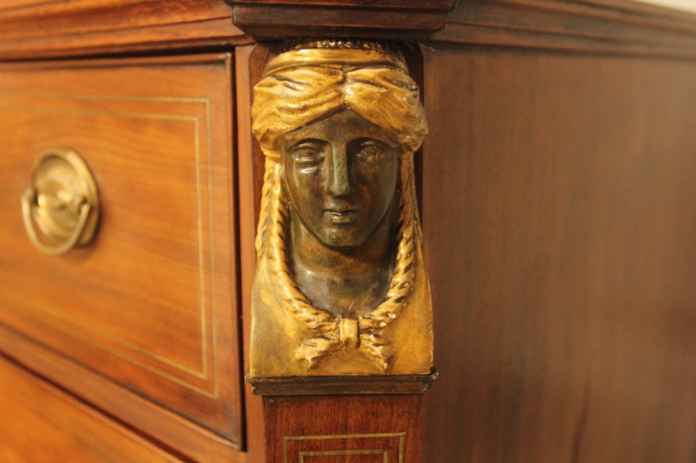 A French 19th-century mahogany tallboy chest of drawers featuring six drawers, brass ring handles, escutcheons, and fluted side pilasters topped with brass busts. View V
