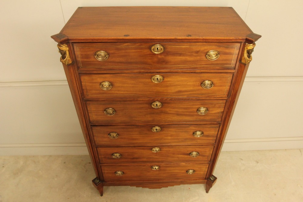 A French 19th-century mahogany tallboy chest of drawers featuring six drawers, brass ring handles, escutcheons, and fluted side pilasters topped with brass busts. View X