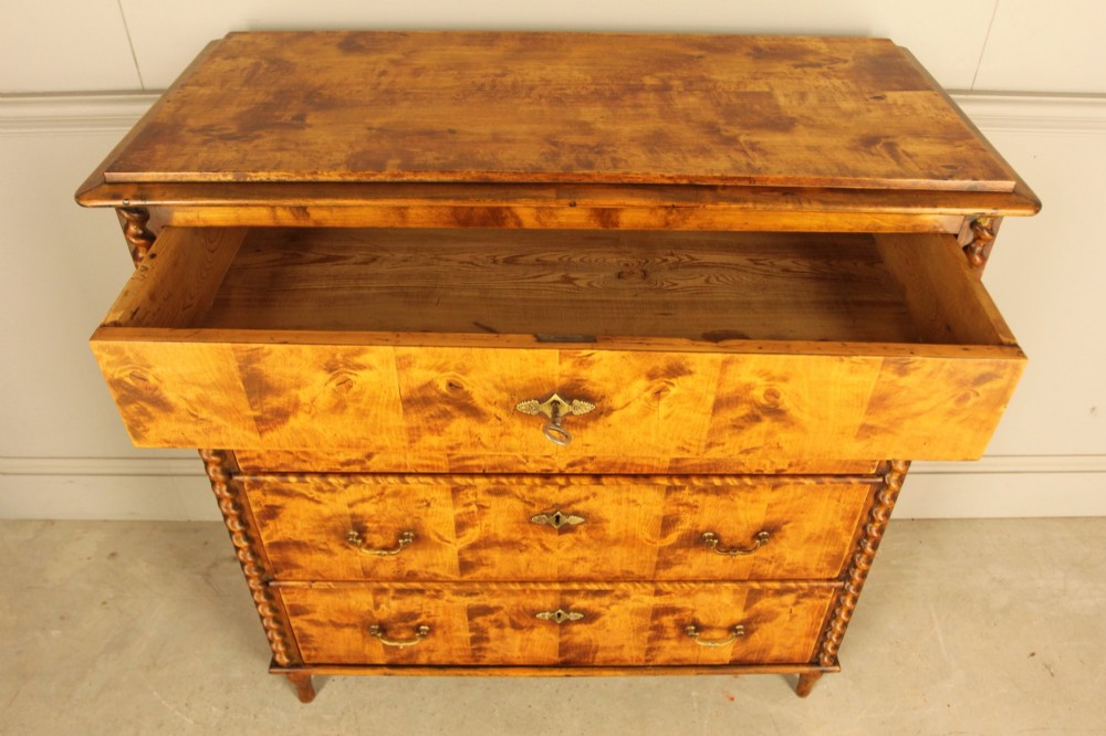 A nineteenth-century Swedish chest of drawers crafted from highly figured flame birch veneer, featuring four full-width drawers with brass drop handles, brass escutcheons, and spiral-twisted side columns. View V