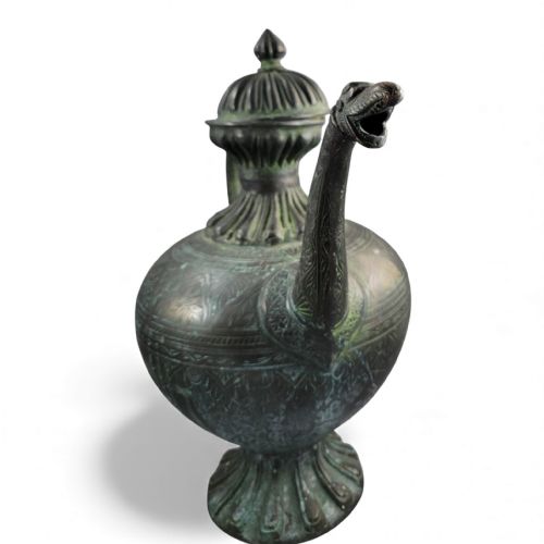 fig 1. An antique dark bronze Indian aftaba ewer featuring an engraved bulbous body, a creature-shaped spout, a fluted base, and a Makara handle.