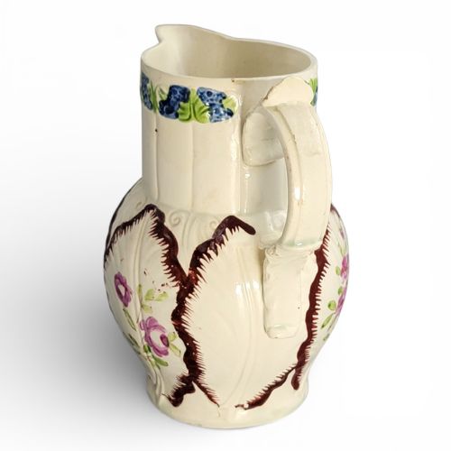 fig 1. An antique cream glazed ceramic jug featuring raised cabbage leaf moulding, hand-painted floral motifs, and a moulded scroll handle.