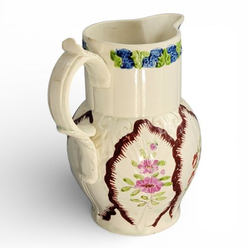 fig 2. An antique cream glazed ceramic jug featuring raised cabbage leaf moulding, hand-painted floral motifs, and a moulded scroll handle.