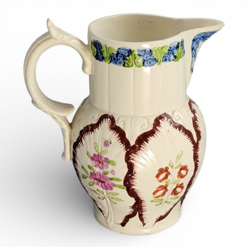 fig 3. An antique cream glazed ceramic jug featuring raised cabbage leaf moulding, hand-painted floral motifs, and a moulded scroll handle.