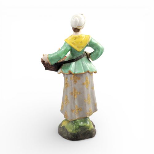 fig 3. An antique Georgian Derby porcelain figurine depicting a female street vendor wearing a green jacket and patterned apron while holding a tray of baked goods.