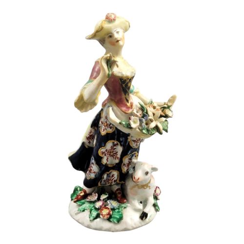 fig 2. An 18th-century Bow porcelain figurine depicting a lady in a patterned skirt and wide-brimmed hat holding flowers alongside a seated lamb.