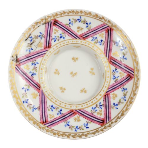 fig 1. A French Neoclassical porcelain covered trembleuse cup and saucer decorated with pink ribbons, blue floral garlands, gold leaf borders, and a cherry-shaped lid finial.