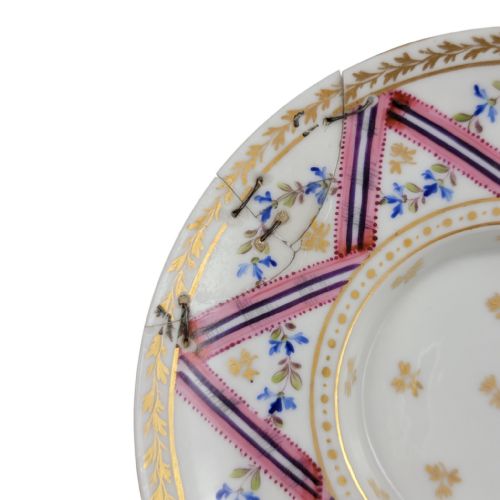 fig 2. A French Neoclassical porcelain covered trembleuse cup and saucer decorated with pink ribbons, blue floral garlands, gold leaf borders, and a cherry-shaped lid finial.