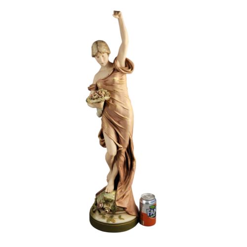fig 1. An Art Nouveau porcelain figure depicting a maiden in flowing drapery with one arm raised aloft and holding flowers at her waist.