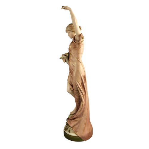 fig 2. An Art Nouveau porcelain figure depicting a maiden in flowing drapery with one arm raised aloft and holding flowers at her waist.