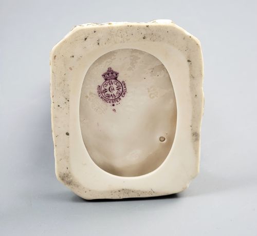 fig 3. A standing porcelain figurine depicting a lady in a floral dress and bonnet with gilded trim on a textured base.