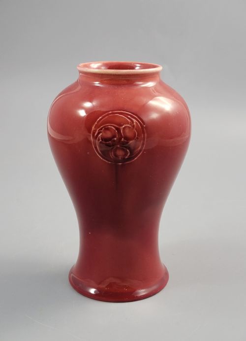 fig 1. A red glazed earthenware vase featuring a baluster shape with an embossed roundel medallion near the rim.