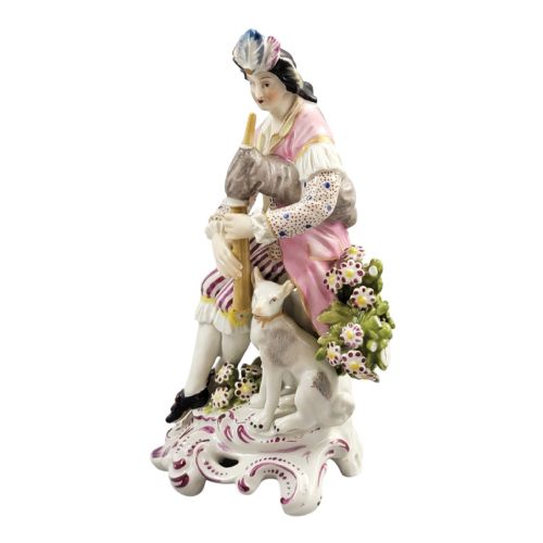 fig 1. An 18th-century Derby soft-paste porcelain figurine featuring a seated bagpiper in a pink coat with a small white dog at his feet on a scrollwork base.