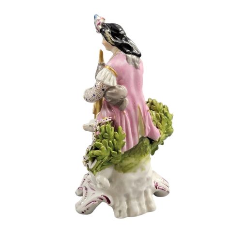 fig 2. An 18th-century Derby soft-paste porcelain figurine featuring a seated bagpiper in a pink coat with a small white dog at his feet on a scrollwork base.