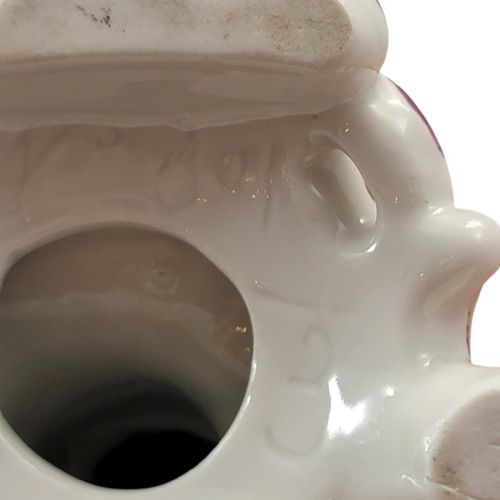 fig 3. An 18th-century Derby soft-paste porcelain figurine featuring a seated bagpiper in a pink coat with a small white dog at his feet on a scrollwork base.