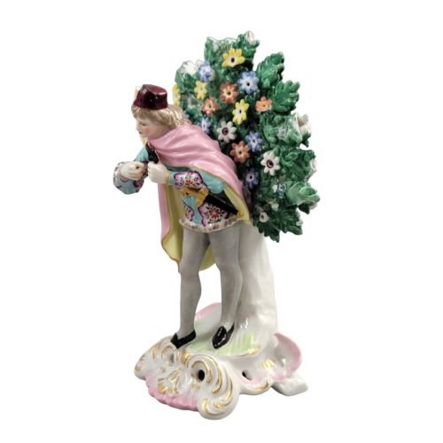 fig 1. A nineteenth-century French Samson porcelain figurine depicting a masked actor in a patterned jacket and cape standing before a flowering green tree backdrop.