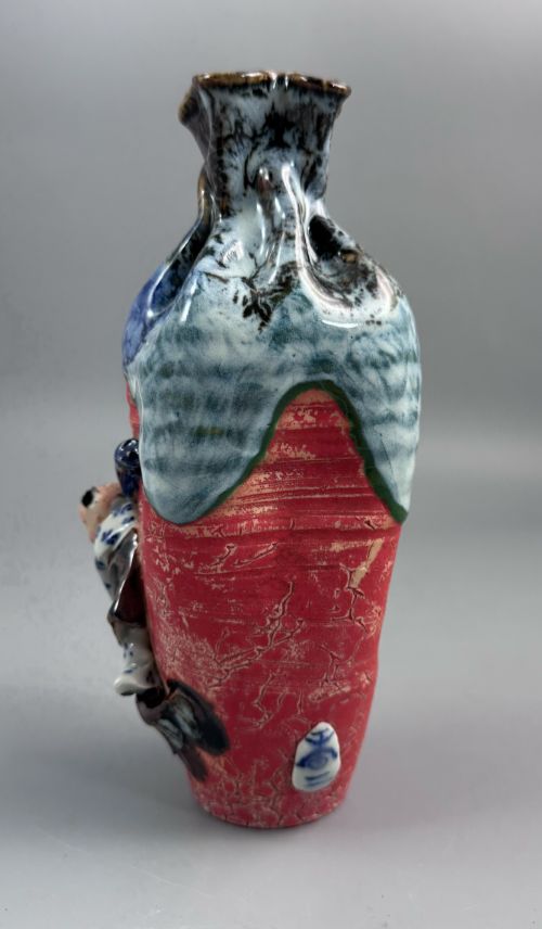 fig 2. A Japanese Sumida Gawa baluster vase featuring a ribbed red surface, a dripping blue flambe glaze at the rim, and a sculpted karako figure on the side.