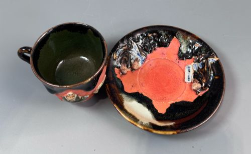 fig 3. A Japanese Sumida Gawa teacup and saucer featuring relief-carved sage figures on a textured red background with a heavy dark flambe glaze.