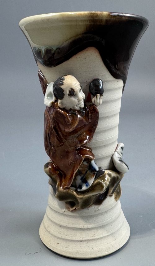 fig 2. A Japanese Sumida Gawa stoneware vase featuring a ribbed cream body, dripping dark glaze along the flared rim, and an applied high-relief figure of a Rakan.