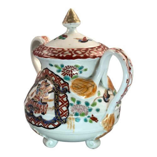 fig 4. A covered Japanese Imari porcelain sugar bowl featuring double side handles, a pointed gilded finial, and hand-painted samurai and floral motifs in red, blue, green, and gold enamels.