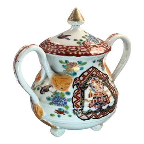 fig 5. A covered Japanese Imari porcelain sugar bowl featuring double side handles, a pointed gilded finial, and hand-painted samurai and floral motifs in red, blue, green, and gold enamels.