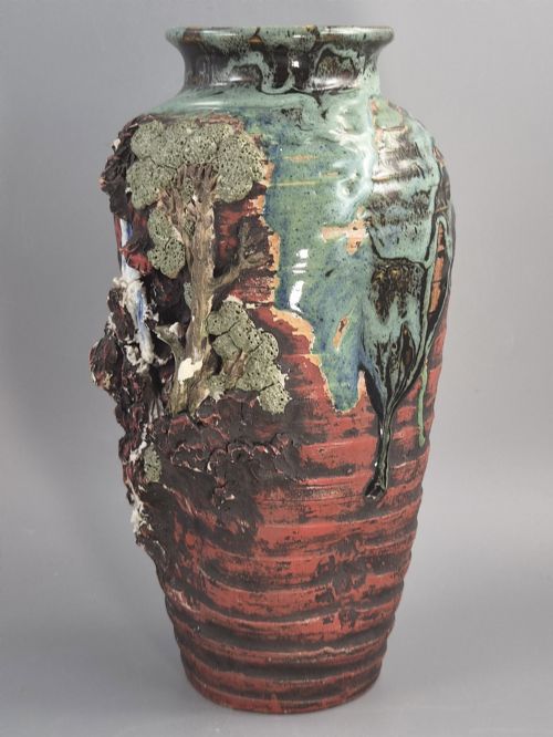 fig 1. A Japanese Sumida Gawa stoneware vase featuring high-relief sculptures of a stag, waterfall, and tree against a ribbed dark red base with a green drip glaze top rim.