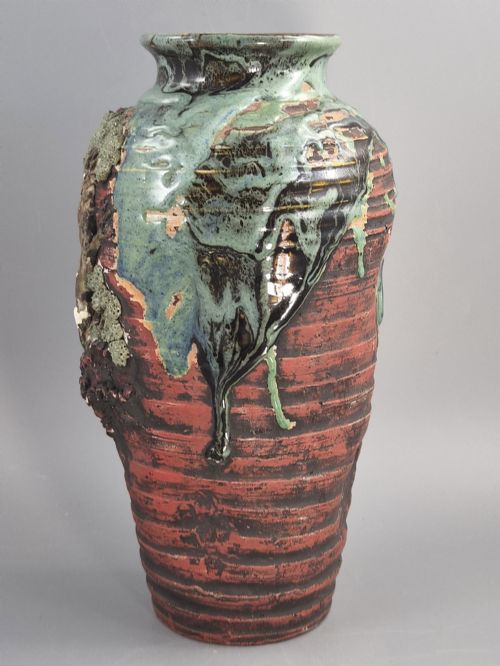 fig 2. A Japanese Sumida Gawa stoneware vase featuring high-relief sculptures of a stag, waterfall, and tree against a ribbed dark red base with a green drip glaze top rim.