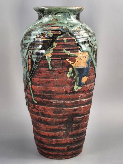 fig 3. A Japanese Sumida Gawa stoneware vase featuring high-relief sculptures of a stag, waterfall, and tree against a ribbed dark red base with a green drip glaze top rim.