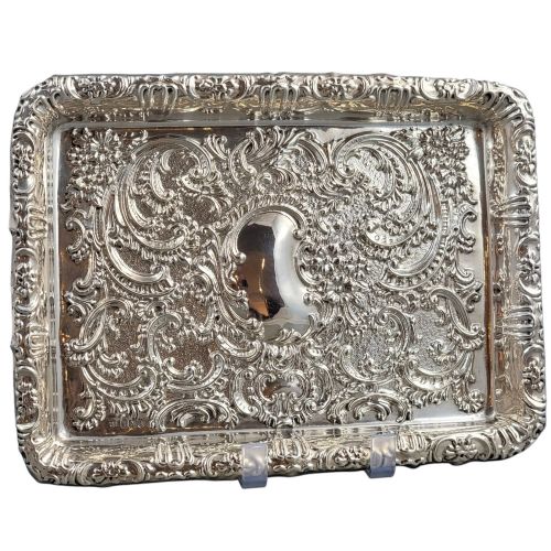 fig 1. A rectangular Edwardian sterling silver card tray with intricate floral repousse scrollwork detailing, a plain central cartouche, and a raised scalloped rim.