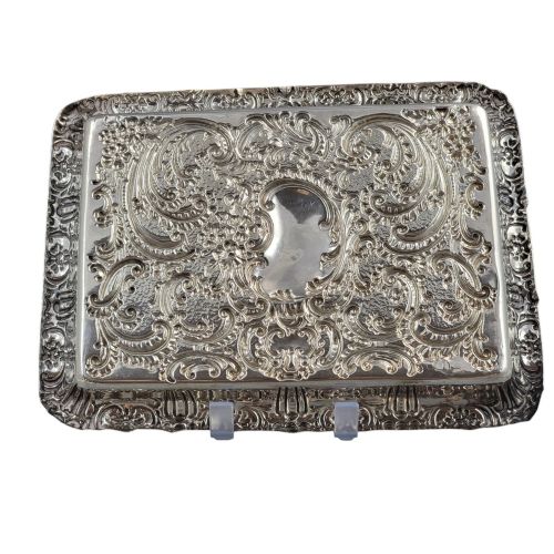 fig 2. A rectangular Edwardian sterling silver card tray with intricate floral repousse scrollwork detailing, a plain central cartouche, and a raised scalloped rim.