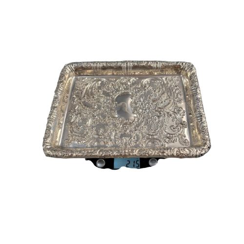 fig 3. A rectangular Edwardian sterling silver card tray with intricate floral repousse scrollwork detailing, a plain central cartouche, and a raised scalloped rim.