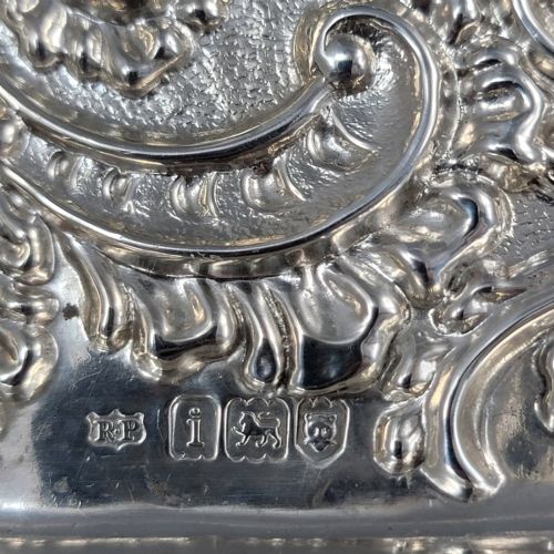 fig 4. A rectangular Edwardian sterling silver card tray with intricate floral repousse scrollwork detailing, a plain central cartouche, and a raised scalloped rim.