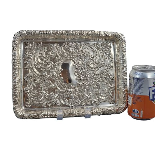 fig 5. A rectangular Edwardian sterling silver card tray with intricate floral repousse scrollwork detailing, a plain central cartouche, and a raised scalloped rim.