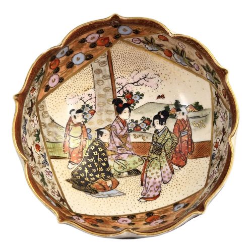 fig 1. A small lobed Japanese Satsuma ceramic bowl with intricate polychrome floral painting and gold gilding, resting on a carved dark wooden base.