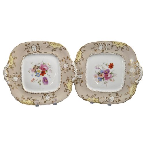 fig 1. A pair of early Victorian Coalport porcelain square dessert dishes featuring hand-painted floral centres, beige borders with gold scrollwork, and moulded twin handles.