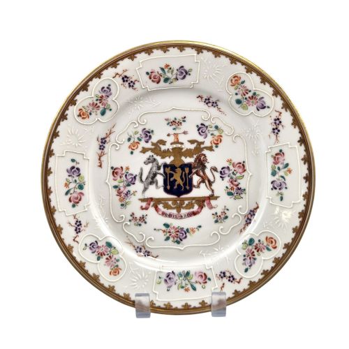fig 5. A pair of circular white porcelain plates featuring a central coat of arms, hand-painted floral sprays, raised enamel details, and gilded rims.