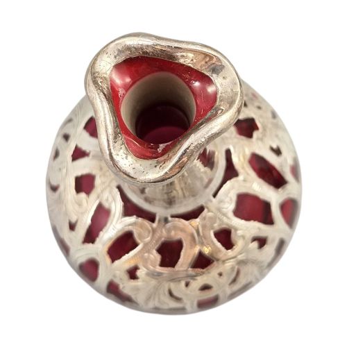 fig 1. A three-piece ruby red glass vanity set featuring floral sterling silver overlay details across two stoppered bottles and a cylindrical beaker.