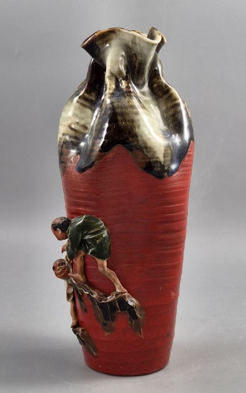 fig 1. A tall Japanese Sumida Gawa ceramic vase featuring a ribbed red body, applied figures of climbing men, and a heavy flambe glaze around a pinched rim.