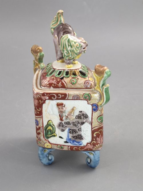 fig 1. A square Japanese Kutani porcelain incense burner featuring a karashishi lion finial on the lid, hand-painted figural panels, and blue elephant-head legs.