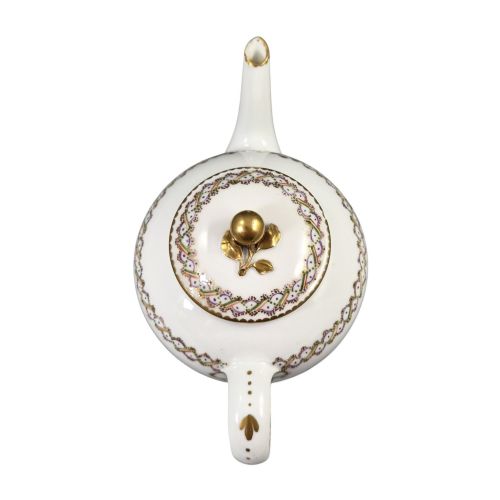 fig 1. A white Sevres porcelain teapot featuring polychrome geometric enamel borders, gilt trim, a rounded body, and a gilded spherical lid finial.