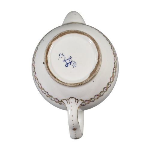 fig 2. A white Sevres porcelain teapot featuring polychrome geometric enamel borders, gilt trim, a rounded body, and a gilded spherical lid finial.