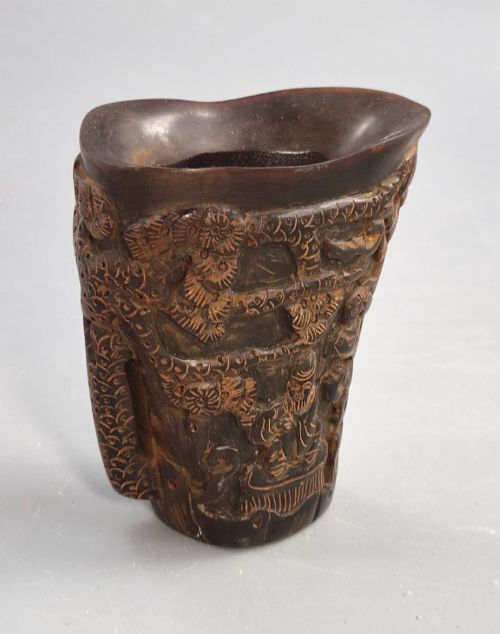 fig 2. A dark brown carved water buffalo horn libation cup featuring relief carvings of immortals standing under pine trees.