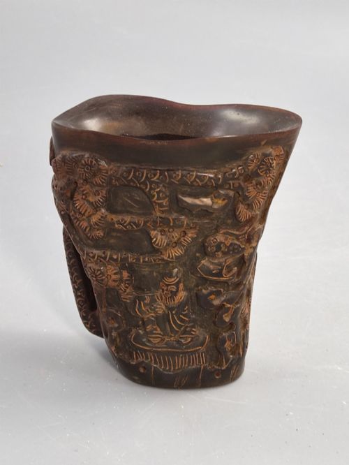 fig 3. A dark brown carved water buffalo horn libation cup featuring relief carvings of immortals standing under pine trees.