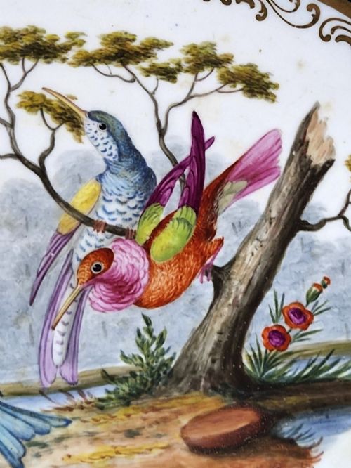 fig 2. An oval porcelain dish featuring a dark cobalt blue rim with gold scrollwork, reticulated handles, floral panels, and a central hand-painted scene of colorful birds perched on branches.