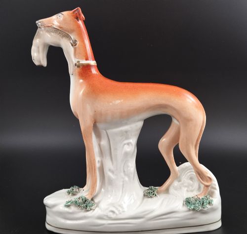 fig 1. A pair of antique Victorian Staffordshire earthenware figures depicting standing orange greyhounds holding grey hares in their jaws on white bases.