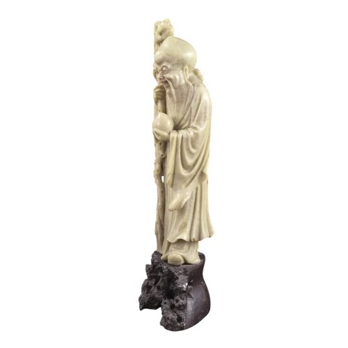 fig 1. A late 19th-century carved pale soapstone figure of Shoulao holding a peach and staff, standing on a dark stone pierced rockwork base.