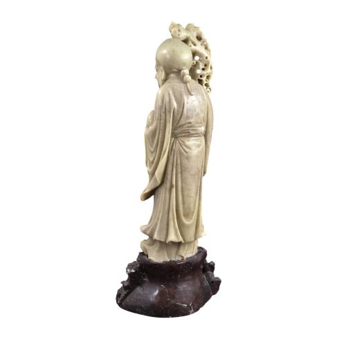 fig 2. A late 19th-century carved pale soapstone figure of Shoulao holding a peach and staff, standing on a dark stone pierced rockwork base.