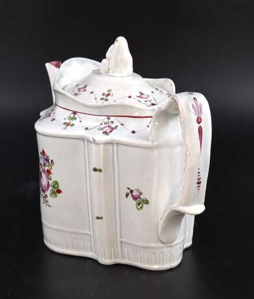 fig 1. An off-white earthenware commode-shaped teapot decorated with hand-painted floral sprays, red borders, and a seated widow finial on the lid.