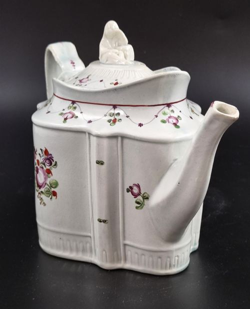 fig 3. An off-white earthenware commode-shaped teapot decorated with hand-painted floral sprays, red borders, and a seated widow finial on the lid.
