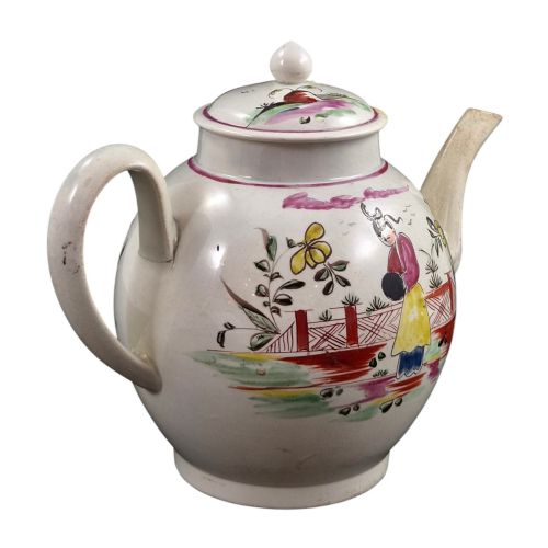fig 2. An 18th-century creamware teapot featuring hand-painted polychrome Chinoiserie figures on a cream glaze background with a curved spout and loop handle.