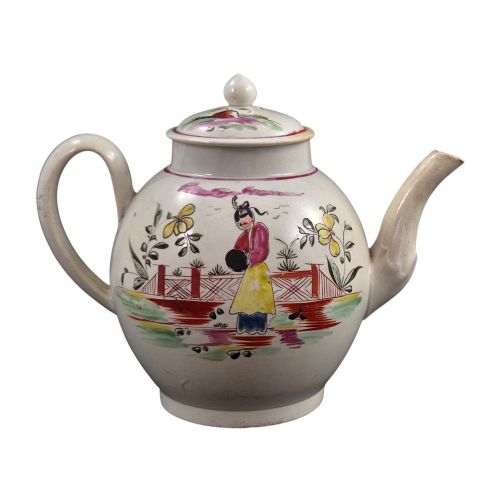 fig 3. An 18th-century creamware teapot featuring hand-painted polychrome Chinoiserie figures on a cream glaze background with a curved spout and loop handle.